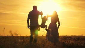 Mom, dad and baby play outdoors. healthy little daughter jumps and flies in arms of mother and father in field at sunset