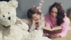 Mom and daughter comfortably lying in bed, reading fairy tales and dreaming