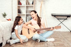 Mom and her daughter are sitting on the floor at home and playing the guitar. They sing to the guitar. stock photography Mom and her daughter are sitting on the floor at home and playing the guitar. They sing to the guitar. stock photography