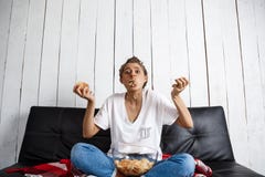 Mooi binnenlands meisje die spaanders eten, lettend op TV, die bij bank zitten Stock Fotografie Mooi binnenlands meisje die spaanders eten, lettend op TV, die bij bank zitten Stock Fotografie