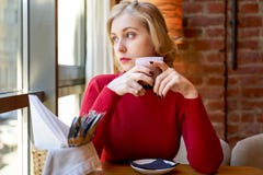 Mooi blondemeisje die uit het venster, die een Kop van koffie houden kijken Peinzende vrouw die over aanstaande gevallen denken stock afbeeldingen Mooi blondemeisje die uit het venster, die een Kop van koffie houden kijken Peinzende vrouw die over aanstaande gevallen denken stock afbeeldingen
