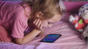 Mooi kind met blond haar, in een roze op voederbak liggen en overhemd die beeldverhalen op haar mum mobiele telefoon kijken Scher stock footage Mooi kind met blond haar, in een roze op voederbak liggen en overhemd die beeldverhalen op haar mum mobiele telefoon kijken Scher stock footage