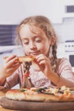 Mooi portret van weinig kindmeisje die van een heerlijke pizza genieten royalty-vrije stock afbeeldingen Mooi portret van weinig kindmeisje die van een heerlijke pizza genieten royalty-vrije stock afbeeldingen