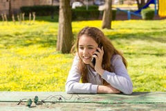 Mooi tienermeisje die door mobiele cellpfonesmartphone bij het de zomerpark spreken stock afbeelding Mooi tienermeisje die door mobiele cellpfonesmartphone bij het de zomerpark spreken stock afbeelding