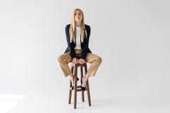 mooie jonge blondevrouw in modieuze kleren die op kruk zitten en camera bekijken royalty-vrije stock foto mooie jonge blondevrouw in modieuze kleren die op kruk zitten en camera bekijken royalty-vrije stock foto