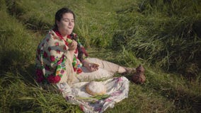 Mooie te zware vrouwenzitting in gras op het gebied die het brood van verse brood en komkommer eten tradities stock footage Mooie te zware vrouwenzitting in gras op het gebied die het brood van verse brood en komkommer eten tradities stock footage