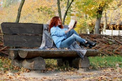 Mooie Vrouw met rood haar in het de herfstpark zit op een bank en leest een boek De achtergrond van de herfst Rode en oranje het stock foto's Mooie Vrouw met rood haar in het de herfstpark zit op een bank en leest een boek De achtergrond van de herfst Rode en oranje het stock foto's