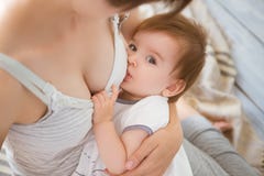 Mother breastfeeding baby in her arms at home. Mom breast feeding her newborn child. Baby eating mother`s milk. Concept of lactat Stock Image Mother breastfeeding baby in her arms at home. Mom breast feeding her newborn child. Baby eating mother`s milk. Concept of lactat Stock Image