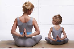 Mother and daughter doing yoga exercise, fitness, gym wearing the same comfortable tracksuits, family sports, sports paired siting