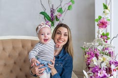 Mother and daughter embrace. Beautiful mother with kid girl sit on a sofa. Studio portrait with flowers. Female model. royalty free stock photography Mother and daughter embrace. Beautiful mother with kid girl sit on a sofa. Studio portrait with flowers. Female model. royalty free stock photography