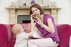 Mother using telephone in living room with baby