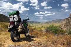Motorcycle enduro traveler with suitcases in mountain valley on the background of the rocky hills Stock Photography Motorcycle enduro traveler with suitcases in mountain valley on the background of the rocky hills Stock Photography