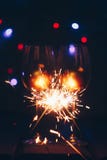 Moussera Bengal tomteblosspinnar i flammor på en svart bakgrund med ljusbokeh- och vinexponeringsglas Nytt år för jultema royaltyfri bild Moussera Bengal tomteblosspinnar i flammor på en svart bakgrund med ljusbokeh- och vinexponeringsglas Nytt år för jultema royaltyfri bild