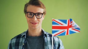 Mouvement lent en gros plan de type de sourire tenant le drapeau britannique ondulant en vent banque de vidéos Mouvement lent en gros plan de type de sourire tenant le drapeau britannique ondulant en vent banque de vidéos