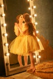 A moça bonita em um vestido de noite do ouro está em um tapete da pele perto de um grande espelho em um quadro com luzes e olhare fotos de stock royalty free A moça bonita em um vestido de noite do ouro está em um tapete da pele perto de um grande espelho em um quadro com luzes e olhare fotos de stock royalty free
