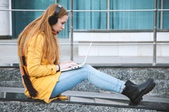 A moça nos fones de ouvido guarda um portátil, sentando-se nas etapas da universidade imagens de stock A moça nos fones de ouvido guarda um portátil, sentando-se nas etapas da universidade imagens de stock