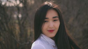 Muchacha asiática joven hermosa que da vuelta a la cámara El viento infla suavemente su pelo almacen de metraje de vídeo Muchacha asiática joven hermosa que da vuelta a la cámara El viento infla suavemente su pelo almacen de metraje de vídeo