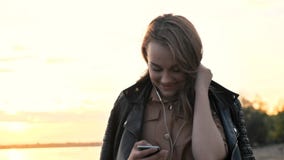 Muchacha atractiva en auriculares usando smartphone en la naturaleza, escuchando la música y hojeando en smartphone almacen de metraje de vídeo Muchacha atractiva en auriculares usando smartphone en la naturaleza, escuchando la música y hojeando en smartphone almacen de metraje de vídeo