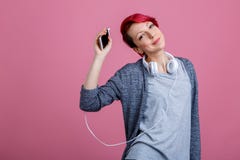 Muchacha con el pelo rojo que escucha la música en los auriculares que aumentan su mano que detiene el teléfono Imagen de archivo Muchacha con el pelo rojo que escucha la música en los auriculares que aumentan su mano que detiene el teléfono Imagen de archivo