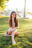 Muchacha del pelo de Brown que pasa el tiempo libre, sentándose en la hierba en el parque, relajándose en la sol fotografía de archivo libre de regalías Muchacha del pelo de Brown que pasa el tiempo libre, sentándose en la hierba en el parque, relajándose en la sol fotografía de archivo libre de regalías