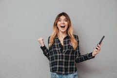 Muchacha emocionada feliz que sostiene el teléfono móvil y que celebra triunfo Foto de archivo libre de regalías Muchacha emocionada feliz que sostiene el teléfono móvil y que celebra triunfo Foto de archivo libre de regalías