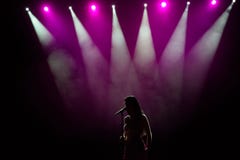Muchacha en el vestido largo que se realiza en etapa Muchacha que canta en la etapa delante de las luces Silueta de la situación imagen de archivo libre de regalías Muchacha en el vestido largo que se realiza en etapa Muchacha que canta en la etapa delante de las luces Silueta de la situación imagen de archivo libre de regalías