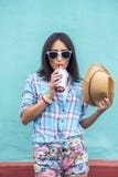 Muchacha en una ciudad con el casquillo en el batido de leche de consumición de la camisa, jugo fresco, gozando, morenita, maquil Fotografía de archivo