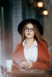 Muchacha hermosa con el sombrero y los vidrios con café y una revista imagen de archivo libre de regalías Muchacha hermosa con el sombrero y los vidrios con café y una revista imagen de archivo libre de regalías