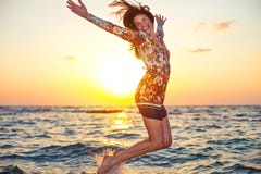 Muchacha hermosa en el vestido colorido que salta en agua del océano en puesta del sol fotos de archivo libres de regalías Muchacha hermosa en el vestido colorido que salta en agua del océano en puesta del sol fotos de archivo libres de regalías