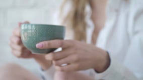 Muchacha hermosa que se sienta en té de consumición de la cama, mirando la cámara y la sonrisa La cámara se está moviendo detrás almacen de video Muchacha hermosa que se sienta en té de consumición de la cama, mirando la cámara y la sonrisa La cámara se está moviendo detrás almacen de video