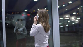 Muchacha joven, hermosa que habla en el teléfono en un terminal de aeropuerto vacío contra la perspectiva de un avión metrajes Muchacha joven, hermosa que habla en el teléfono en un terminal de aeropuerto vacío contra la perspectiva de un avión metrajes