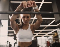 Muchacha morena joven atlética vestida en la ropa de deportes que tiene resto al lado del barbell en el gimnasio moderno imagenes de archivo Muchacha morena joven atlética vestida en la ropa de deportes que tiene resto al lado del barbell en el gimnasio moderno imagenes de archivo
