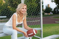 Muchacha rubia feliz con fútbol americano. Mujer joven hermosa alegre sonriente que se sienta en el banco. Al aire libre. Fan del Foto de archivo libre de regalías Muchacha rubia feliz con fútbol americano. Mujer joven hermosa alegre sonriente que se sienta en el banco. Al aire libre. Fan del Foto de archivo libre de regalías