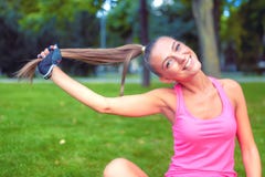 Muchacha rubia sonriente que juega con el pelo mientras que se resuelve en parque fotos de archivo Muchacha rubia sonriente que juega con el pelo mientras que se resuelve en parque fotos de archivo