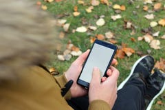 Muchacho en la chaqueta marrón que mira un smartphone fotos de archivo libres de regalías Muchacho en la chaqueta marrón que mira un smartphone fotos de archivo libres de regalías