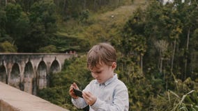 Muchacho europeo lindo feliz del tiro medio pequeño que toma la foto del smartphone en Ella Nine Arches Bridge el las vacaciones almacen de video Muchacho europeo lindo feliz del tiro medio pequeño que toma la foto del smartphone en Ella Nine Arches Bridge el las vacaciones almacen de video