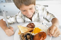 Muchacho joven que come el desayuno frito malsano foto de archivo libre de regalías Muchacho joven que come el desayuno frito malsano foto de archivo libre de regalías