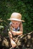 Muchacho lindo con subida que intenta del sombrero de paja en un árbol Imagen de archivo Muchacho lindo con subida que intenta del sombrero de paja en un árbol Imagen de archivo