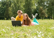 Muchacho y muchacha que se sientan en hierba con el ordenador portátil, en línea en parque Dos estudiantes sonrientes de los adol Imagen de archivo Muchacho y muchacha que se sientan en hierba con el ordenador portátil, en línea en parque Dos estudiantes sonrientes de los adol Imagen de archivo