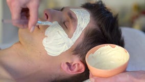 Mud facial mask of man in spa salon. Face massage .
