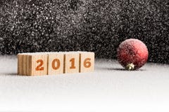 muestra 2016 en los cubos de madera y la bola roja de la Navidad que mienten en una nieve Imágenes de archivo libres de regalías muestra 2016 en los cubos de madera y la bola roja de la Navidad que mienten en una nieve Imágenes de archivo libres de regalías