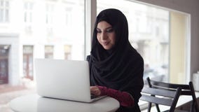 Mujer atractiva en el hijab que busca para algo en Internet Retrato de la mujer musulmán joven sonriente que trabaja en moderno almacen de video Mujer atractiva en el hijab que busca para algo en Internet Retrato de la mujer musulmán joven sonriente que trabaja en moderno almacen de video