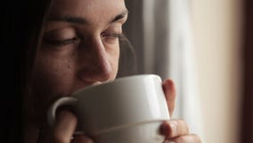 Mujer atractiva joven que se sienta cerca de la ventana y del té de consumición Mujer atractiva joven que se sienta cerca de la ventana y del té de consumición