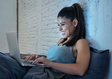 Mujer atractiva que sonríe en el ordenador mientras que mira medios en su ordenador portátil tarde en la noche foto de archivo Mujer atractiva que sonríe en el ordenador mientras que mira medios en su ordenador portátil tarde en la noche foto de archivo