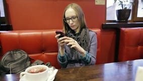 Mujer bonita en vidrios usando el app en smartphone en café que sonríe y que manda un SMS en el teléfono móvil Casual joven hermo metrajes Mujer bonita en vidrios usando el app en smartphone en café que sonríe y que manda un SMS en el teléfono móvil Casual joven hermo metrajes