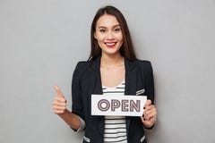 Mujer de negocios feliz que sostiene el letrero abierto y que muestra el pulgar para arriba imagen de archivo libre de regalías Mujer de negocios feliz que sostiene el letrero abierto y que muestra el pulgar para arriba imagen de archivo libre de regalías