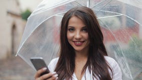Mujer de negocios joven hermosa usando smartphone en la calle en el tiempo lluvioso, sonrisa, celebrando el paraguas Ella que mir almacen de video Mujer de negocios joven hermosa usando smartphone en la calle en el tiempo lluvioso, sonrisa, celebrando el paraguas Ella que mir almacen de video
