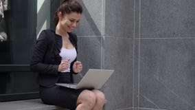 Mujer emocionada que celebra resultados en el ordenador portátil que se sienta fuera de oficina almacen de metraje de vídeo Mujer emocionada que celebra resultados en el ordenador portátil que se sienta fuera de oficina almacen de metraje de vídeo