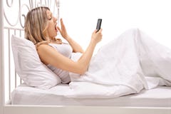 Mujer en la cama que mira el teléfono móvil y que bosteza fotos de archivo libres de regalías Mujer en la cama que mira el teléfono móvil y que bosteza fotos de archivo libres de regalías