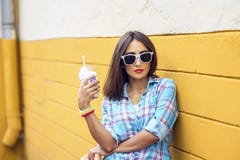 Mujer en la ciudad en el fondo de una pared amarilla, sosteniendo el batido de leche, jugo fresco en vidrios, camisa que lleva co Fotografía de archivo